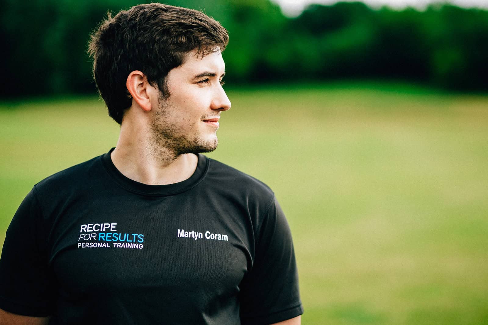 Personal trainer wearing a Recipe For Results jacket standing outdoors on a grassy field, representing professional mobile personal training services in Essex.