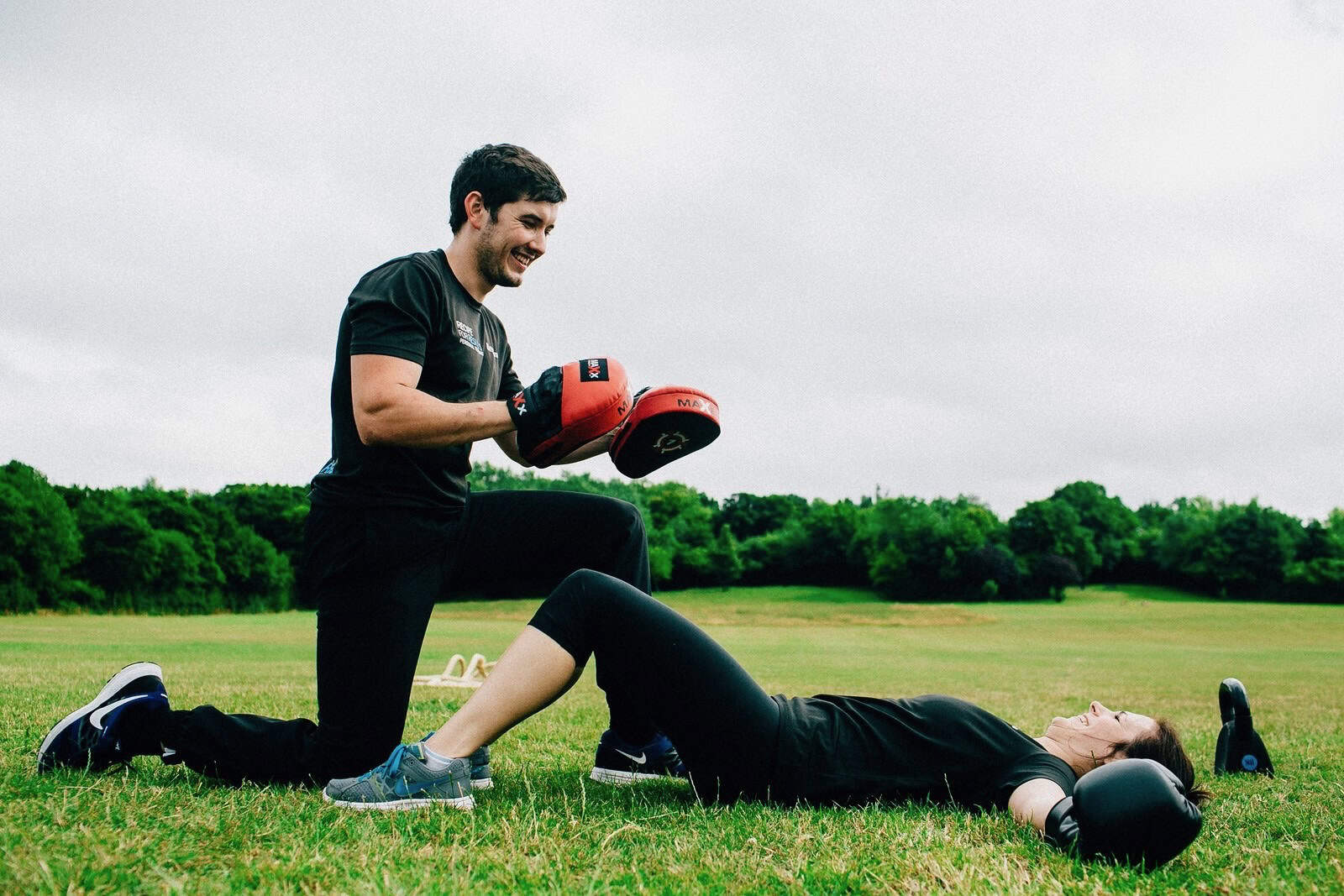 Personal Trainer holding pads for client during an outdoor boxing workout in Essex park